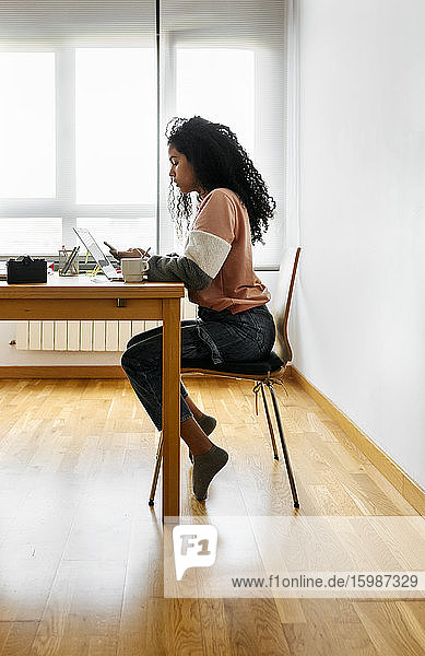 Young woman working from home using laptop and smartphone