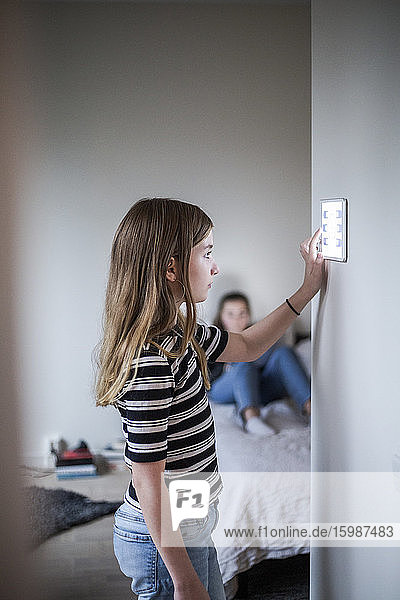 Girl using digital tablet on wall with sister in background at smart home