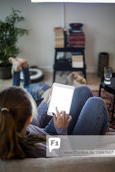 Teenager girl using digital tablet while sitting on sofa at home