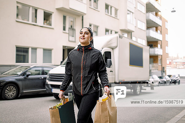 Junge Lieferfrau trägt Einkaufstüten  während sie in der Stadt auf der Straße geht