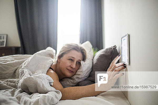 Frau benutzt digitales Tablett an der Wand  während sie im Bett liegt