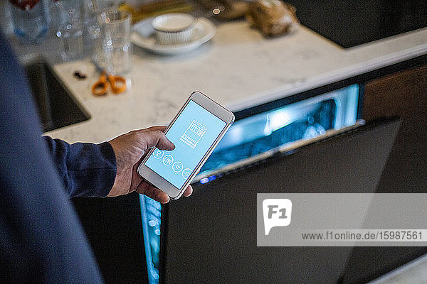 Ausgeschnittenes Bild eines Mannes  der eine mobile App gegen einen Geschirrspüler im Smart Home benutzt