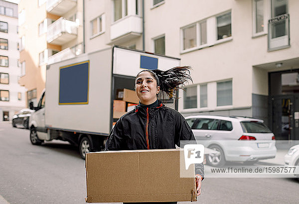 Zuversichtliche junge Zustellerin mit Karton auf der Straße in der Stadt