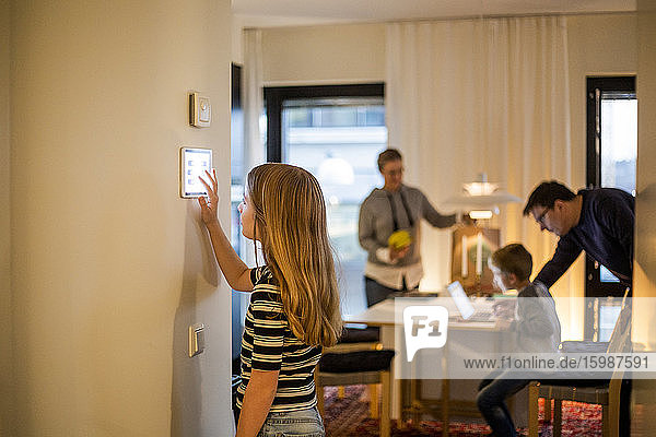 Mädchen benutzt digitales Tablett an der Wand mit Familie im Hintergrund im Smart Home