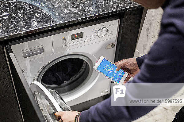 Ausgeschnittenes Bild eines Mannes  der die Waschmaschine mit einer mobilen App im Smart Home steuert