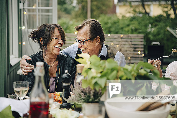 Lächelnder älterer Mann und lächelnde ältere Frau genießen Dinnerparty  während sie im Garten am Esstisch sitzen