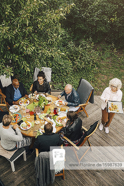 Schrägaufnahme einer Frau  die älteren Freunden während einer Gartenparty im Hinterhof am Esstisch sitzt