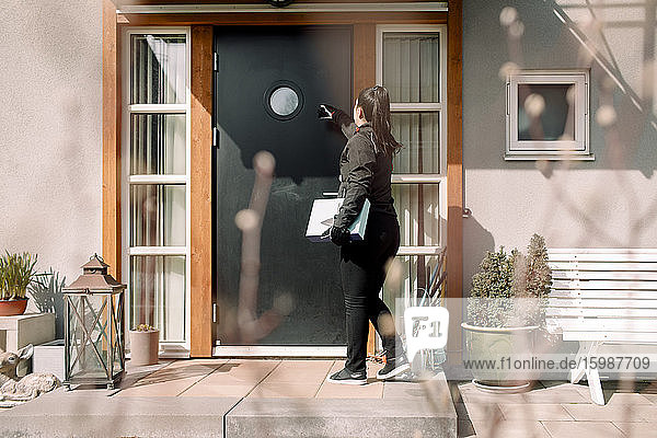 Junge Botenfrau mit Paket am Eingang des Hauses
