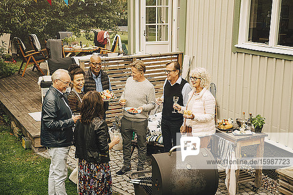 Lächelnde ältere männliche und weibliche Freunde unterhalten sich bei einer Dinnerparty im Hinterhof