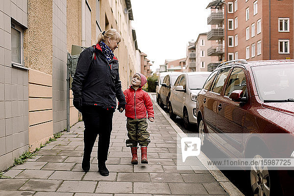 Großmutter und Enkel in voller Länge in warmer Kleidung auf einem Fußweg in der Stadt