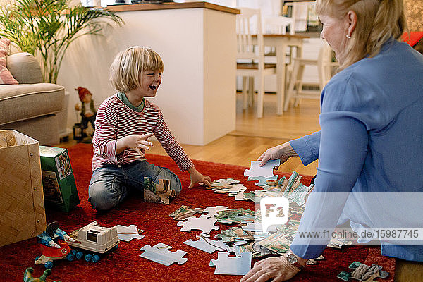 Fröhlicher Junge spielt Puzzle mit Großmutter im Wohnzimmer