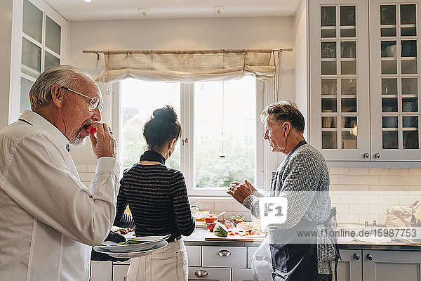 Man eating watermelon while friends talking in kitchen