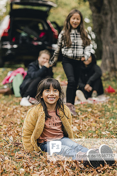 Porträt eines lächelnden Mädchens  das beim Picknick auf Herbstlaub sitzt