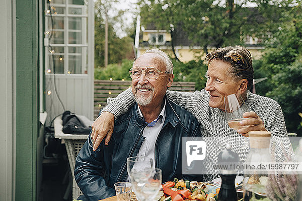 Smiling male friends sitting at dining table enjoying dinner party in back yard
