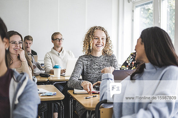 Smiling female friends talking while sitting in classroom