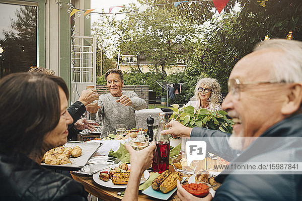 Glückliche ältere männliche und weibliche Freunde genießen die Dinnerparty  während sie am Esstisch im Hinterhof sitzen