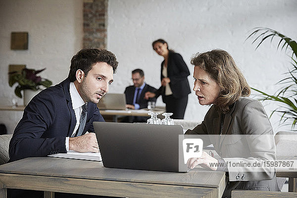 Ältere Anwältin diskutiert mit jungem Geschäftsmann über Laptop während eines Treffens im Büro