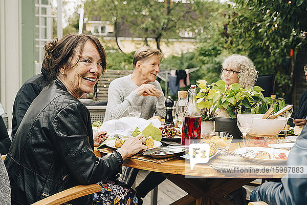 Porträt einer lächelnden älteren Frau  die mit männlichen und weiblichen Freunden am Esstisch sitzt und eine Dinnerparty genießt