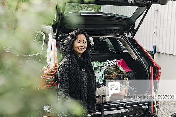 Porträt einer lächelnden Frau mittleren Alters  die an einem Elektroauto steht