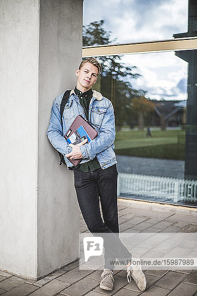Portrait of confident university student leaning on wall