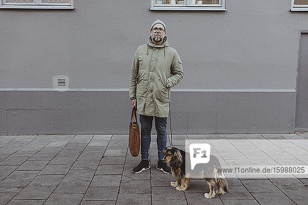 Mittlerer erwachsener Mann in voller Länge mit Hund gegen Gebäude in der Stadt stehend