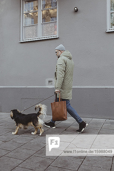 Seitenansicht in voller Länge eines Mannes mit Hund auf einem Fußweg in der Stadt