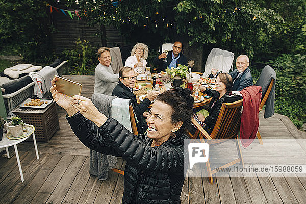 Lächelnde ältere Frau  die während der Dinnerparty mit Freunden am Esstisch im Hinterhof sitzt