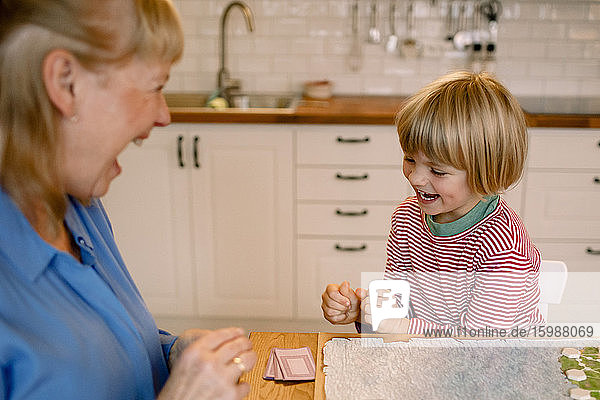 Happy grandson playing board game with grandmother at home