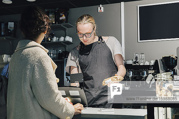 Kunde steht mit transsexueller Kassiererin an der Kasse im beleuchteten Café