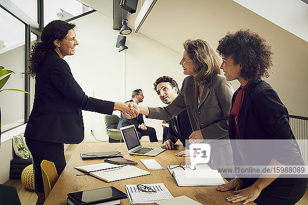 Smiling businesswoman greeting senior female lawyer at conference table during meeting in office