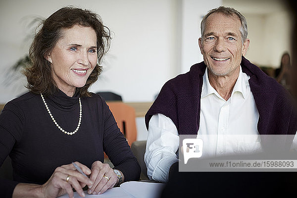 Lächelnde ältere Frau sitzt mit einem Mann während eines Treffens in einer Anwaltskanzlei