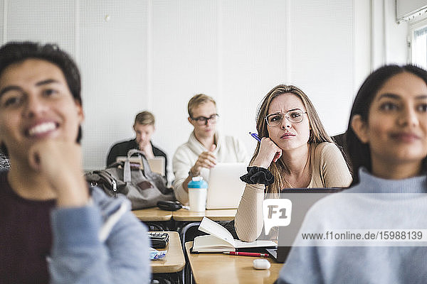 Junge Frau mit Freunden hört zu  während sie im Klassenzimmer sitzt