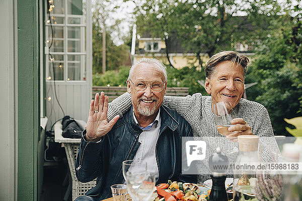 Glückliche männliche Freunde sitzen am Esstisch und genießen die Dinnerparty im Hinterhof