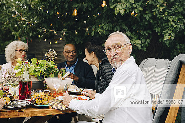 Porträt eines lächelnden älteren Mannes  der mit Freunden bei einem Abendessen am Esstisch sitzt