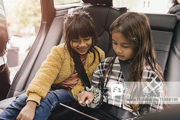 Sisters using digital tablet while sitting in electric car