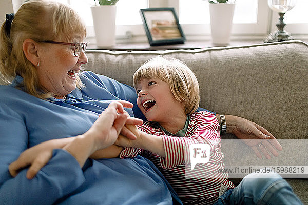 Verspielter Junge mit Großmutter auf dem Sofa im Wohnzimmer zu Hause