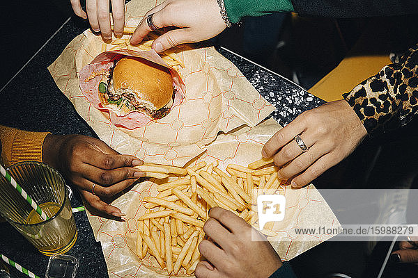 Schrägaufnahme von Freunden  die Burger und Pommes Frites am Tisch im Café essen