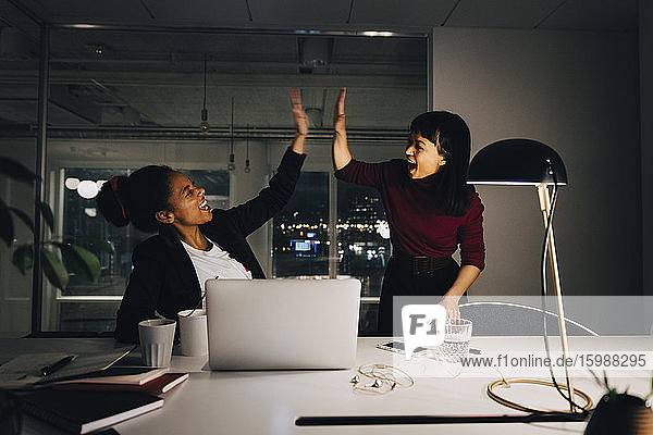 Cheerful female entrepreneurs giving high-five while working late in office