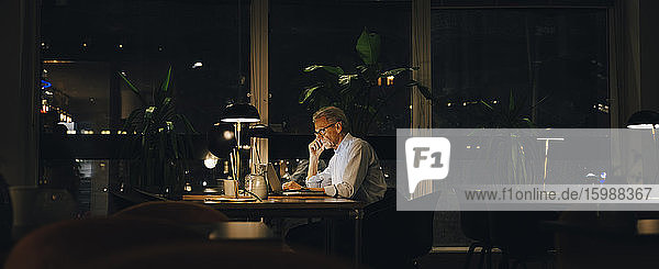 Seitenansicht eines älteren männlichen Unternehmers  der spät in einem dunklen Coworking Space arbeitet