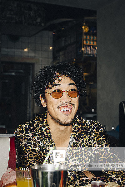 Lächelnder Mann mit Sonnenbrille  der bei geselligem Beisammensein im Restaurant wegschaut
