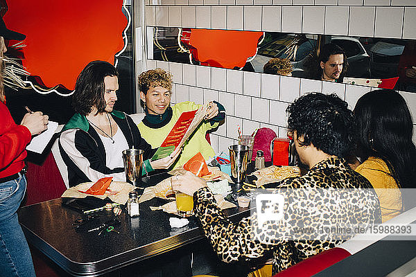 Männliche und weibliche Freunde unterhalten sich  während sie in einem Café am Tisch sitzen und der Kellnerin Essen bestellen