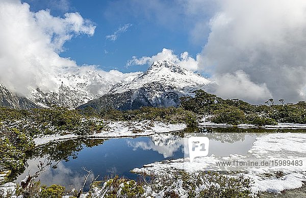 Kleiner Bergsee mit Spiegelung  Ausblick auf wolkenverhangene Berge  Schnee am Gipfel des Key Summit  Mt. Christina  Fiordland Nationalpark  Westküste  Südinsel  Neuseeland  Ozeanien