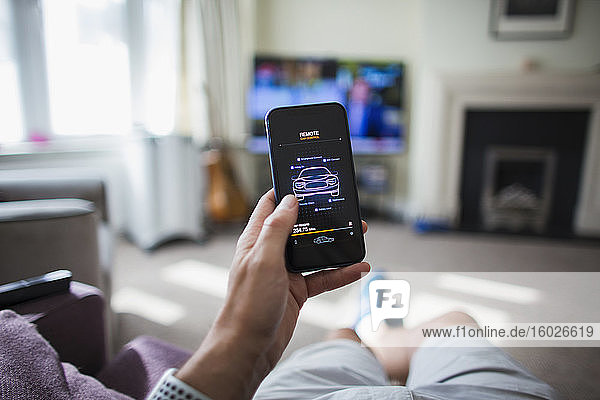 POV Mann prüft Fernsteuerung des Autos auf Smartphone im Wohnzimmer