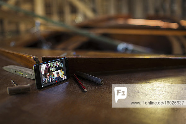 Video-Chat unter Kollegen auf dem Bildschirm eines Smartphones auf einem Holzboot