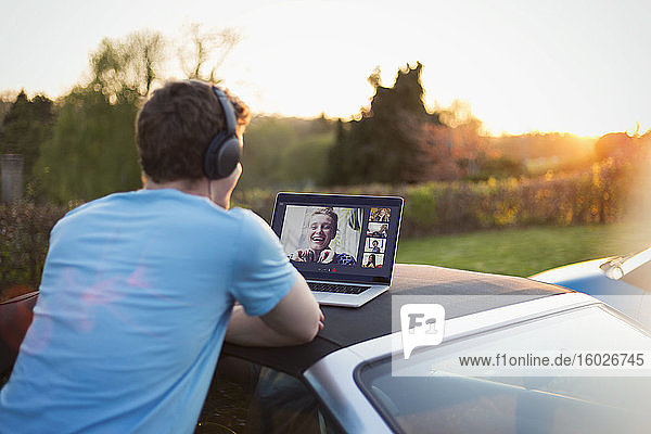 Mann mit Kopfhörern und Laptop beim Video-Chat mit Freunden auf dem Autodach