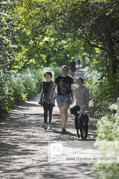 Mutter und Söhne mit Hund auf sonnigem Parkweg