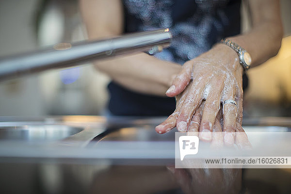 Nahaufnahme einer Frau  die sich an der Küchenspüle die Hände mit Seife wäscht