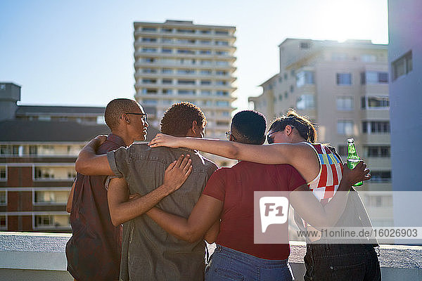 Junge Freunde umarmen sich auf dem sonnigen Balkon auf dem städtischen Dach
