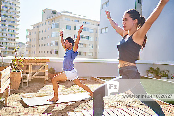 Junges Paar praktiziert Yoga auf sonnigem städtischen Dachbalkon