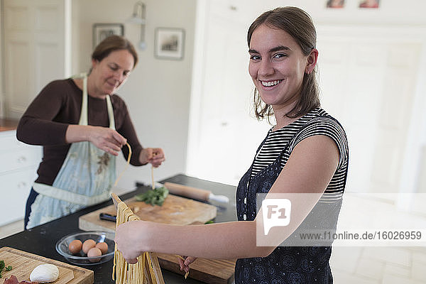 Portrait happy teenage girl making homemade pasta with mother at home